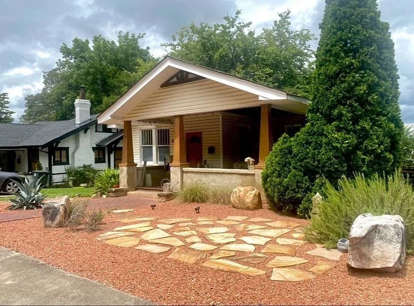 Craftsman-style home with stone path and landscaped yard featuring shrubs and decorative rocks.
