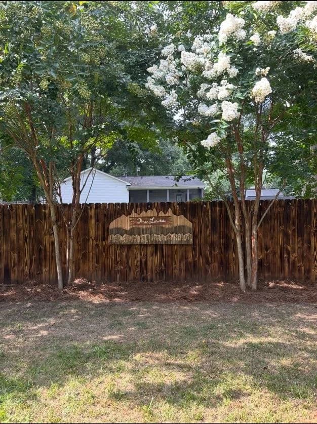 Wooden fence with a sign and blooming white crepe myrtle trees in a residential yard.