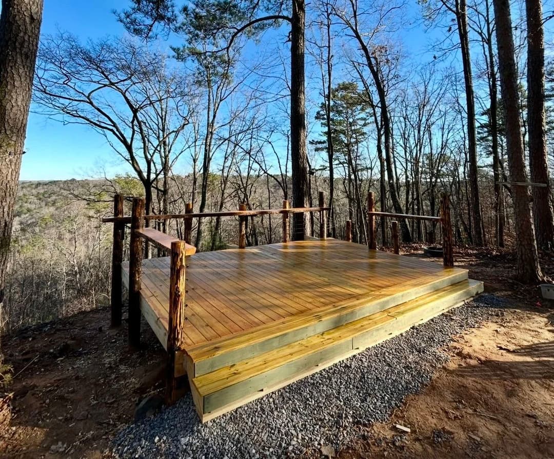 Wooden deck platform surrounded by trees in a scenic forest setting. Perfect for outdoor gatherings.