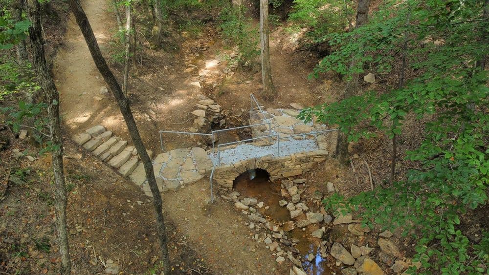 Scenic stone bridge over a creek surrounded by lush greenery and walking path.